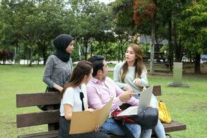 joven asiático malayo chino hombre mujer al aire libre parque libro archivo carpeta ordenador portátil computadora teléfono sentar estar estudiar mezclarse foto