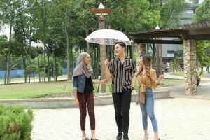 Young Asian Malay man woman outdoor green park walk talk discuss mingle under umbrella photo