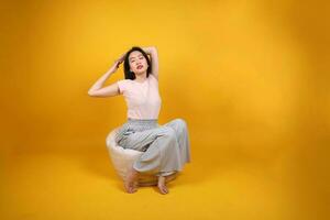 Beautiful young south east Asian woman sits on a white beanbag seat orange yellow color background pose fashion style elegant beauty mood expression rest relax exercise stretch yoga photo