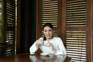 Young asian woman sit at rustic cafe holding cup drink coffee look front at camera photo