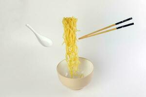 Yellow noodle soup elevated flying suspended in air bowl spoon and chopstick on white background photo