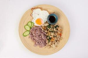 Thai fusion stair fried chicken with Thai basil and cashew nut with health brown rice fried egg sauce cucumber on woody plate over white background photo