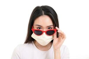 Beautiful young south east Asian woman peaking over wearing red frame dark sunglass three ply anti virus surgical face mask pose fashion style white background photo