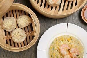 Prawn shrimp shaomai Xiao long bao dim sum dumpling chicken prawn fish seafood vegetable in bamboo steamer fried rice on plate sauce chopsticks soup spoon over rustic background photo