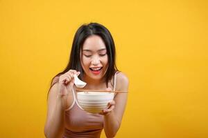 Beautiful young south east Asian woman holding chines empty chopstick Chinese soup spoon bowl utensil pretend acting posing see eat taste smell feed offer satisfaction yummy yellow orange background photo