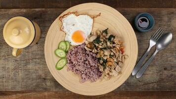 Thai fusion stair fried chicken with Thai basil and cashew nut with health brown rice fried egg sauce cucumber on woody plate over rustic wood background fork spoon photo