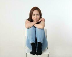 Young attractive Asian chinese malay woman pose face body expression mode emotion on white background think worry sitting legs up chin on keens sad photo