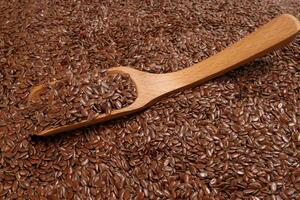 Flex seed flaxseed closeup wooden scoop spoon laid on top with pile of seeds photo