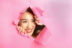 Young beautiful Asian woman expression through torn paper hole photo