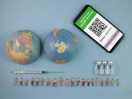 Miniature human figure figurine male female doll row vaccine passport digital paper book bottle medical injection syringe needle world map globe border copy text sign space on blue paper background photo