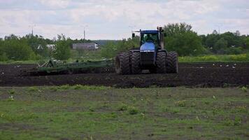 bleu tracteur avec double roues tirant disque herse avec rouleau panier et tournant droite à printemps journée avec lent mouvement video