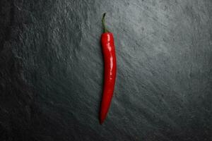 Red hot chilli pepper on dark black rough slate stone surface background photo