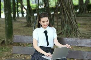 Young asian chinese woman outdoor on park bench use laptop computer think read look happy wonder smile look photo