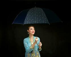 Asian woman in tractional kebaya carrying umbrella on black background photo