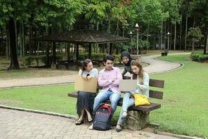 Young asian malay chinese man woman outdoor on park bench study talk discuss point laptop file book photo