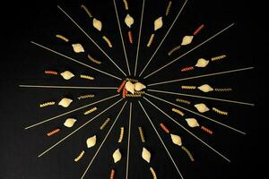 dry raw spaghetti conchiglie seashells fusilli cork screw color pasta laid on black background sunray glow pattern concept photo
