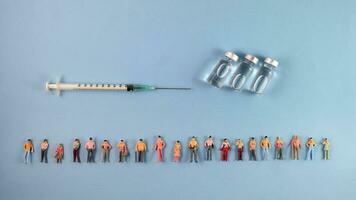 Miniature human figure figurine male female doll row line vaccine bottle medical injection syringe needle border copy text sign space on blue paper background photo