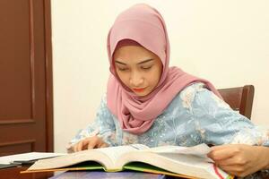 young Asian Malay muslim woman wearing headscarf at home office student sit at table computer read book file paper study work photo