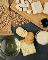 Soyabeans products soya beans flowing bamboo sieve wooden board on jute black stone slate background curd tofu oil milk sauce biscuit cookies photo