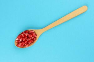 Red Pomegranate seed wooden spoon blue paper background photo