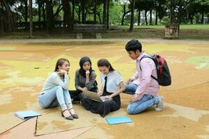 Young asian malay chinese man woman outdoor park sit on ground study talk discuss point laptop file book backpack mingle fun meet photo