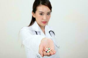 Asian doctor holding medicine capsule tablets pills on palm of hand photo