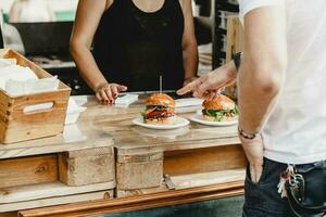 hombre elige hamburguesas a un hamburguesa banquete. cena hamburguesa comida banquete fiesta. grande hamburguesa en manos a calle comida al aire libre festival foto