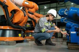 en el robots depósito, un hembra ingeniero inspecciona el eléctrico sistema de cada robótica brazo, antes de entregando a el cliente. foto