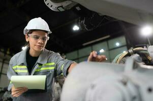 A female engineer checking documented items after installing a program on a robotic arm in a robotic warehouse and test the operation photo