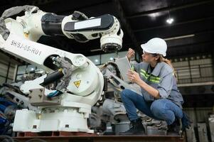 un hembra ingeniero instala un programa en un robótica brazo en un robot depósito. y prueba el operación antes de enviando el máquina a el cliente. foto