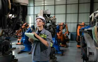 A female engineer checking documented items after installing a program on a robotic arm in a robotic warehouse and test the operation photo