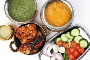 Spicy red Chicken grilled tikka tandoori nan bread green spinach curry yogurt sauce dal tomato cucumber onion salad set in metal stainless steel brass copper pot on white background photo