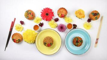 Colorful flower decorated moon cake Chinese mid autumn festival tea in small white teacup chopsticks plates blue yellow violet chrysanthemum mum red daisy flower on white background photo