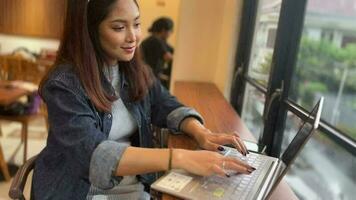 un adorable asiatique femme est travail avec sa portable dans une café video