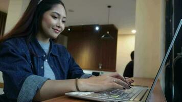 een aanbiddelijk Aziatisch vrouw is werken met haar laptop in een cafe video