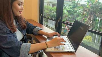un adorable asiático mujer es trabajando con su ordenador portátil en un café video