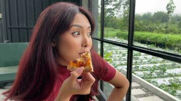 skön asiatisk kvinnor njut av äter pizza i Kafé ser utanför video