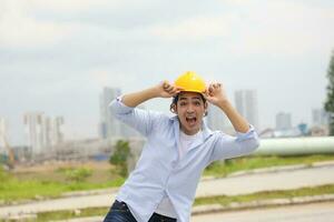 Asian man malay worker engineer management hard hat safety helmet at construction site stand happy joy mouth open hand on hat photo