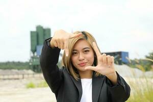 asiático mujer chino malayo trabajador ingeniero administración a construcción sitio marco cara con mano dedo foto
