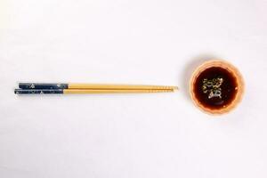 Bamboo wooden chopsticks and chili soya sauce in small ceramic bowl dish on white background photo