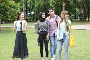 joven asiático malayo chino hombre mujer al aire libre parque caminar estar estudiar hablar discutir punto ordenador portátil archivo libro mochila foto