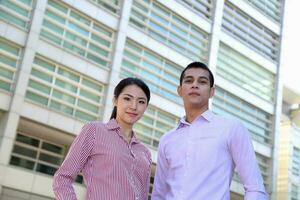 Young south east Asian middle eastern man woman business colleague in front of a tall building look forward at camera photo