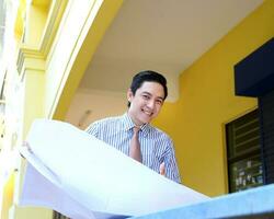 South East Asian young Malay Chinese man wearing formal tie looking at blueprint at outdoor construction site photo