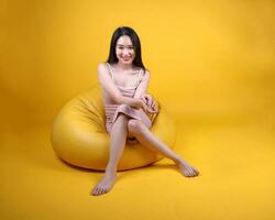 hermosa joven sur este asiático mujer sentar en un amarillo naranja bolsa de frijoles asiento color antecedentes actitud Moda estilo elegante belleza estado animico foto