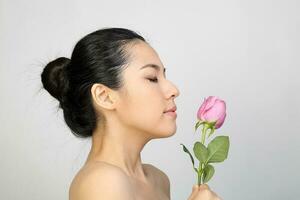 Young beautiful Southeast Asian woman beauty fashion makeup light grey white background holding rose flower smell feel eyes closed photo