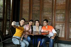 Group young asian malay man woman at rustic wooden cafe table meet talk discuss business study selfie self portrait hand smart phone photo