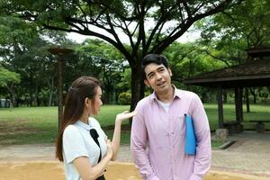 joven asiático malayo chino hombre mujer al aire libre parque caminar estar estudiar hablar discutir ordenador portátil archivo libro mochila actitud trastornado discutir foto