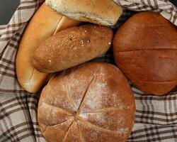 recién horneado un pan pan bollo rodar redondo largo mezcla verdad envuelto en a cuadros cocina tela servilleta toalla trigo flor petróleo agua sal huevos laminación alfiler pizarra Roca terminado negro antecedentes foto