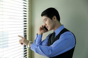 Southeast Asian young office business man in formal wear looking through window talking on phone photo