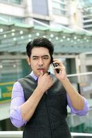 Southeast Asian young office business man wearing vest talk on phone thinking expression outdoor premises photo